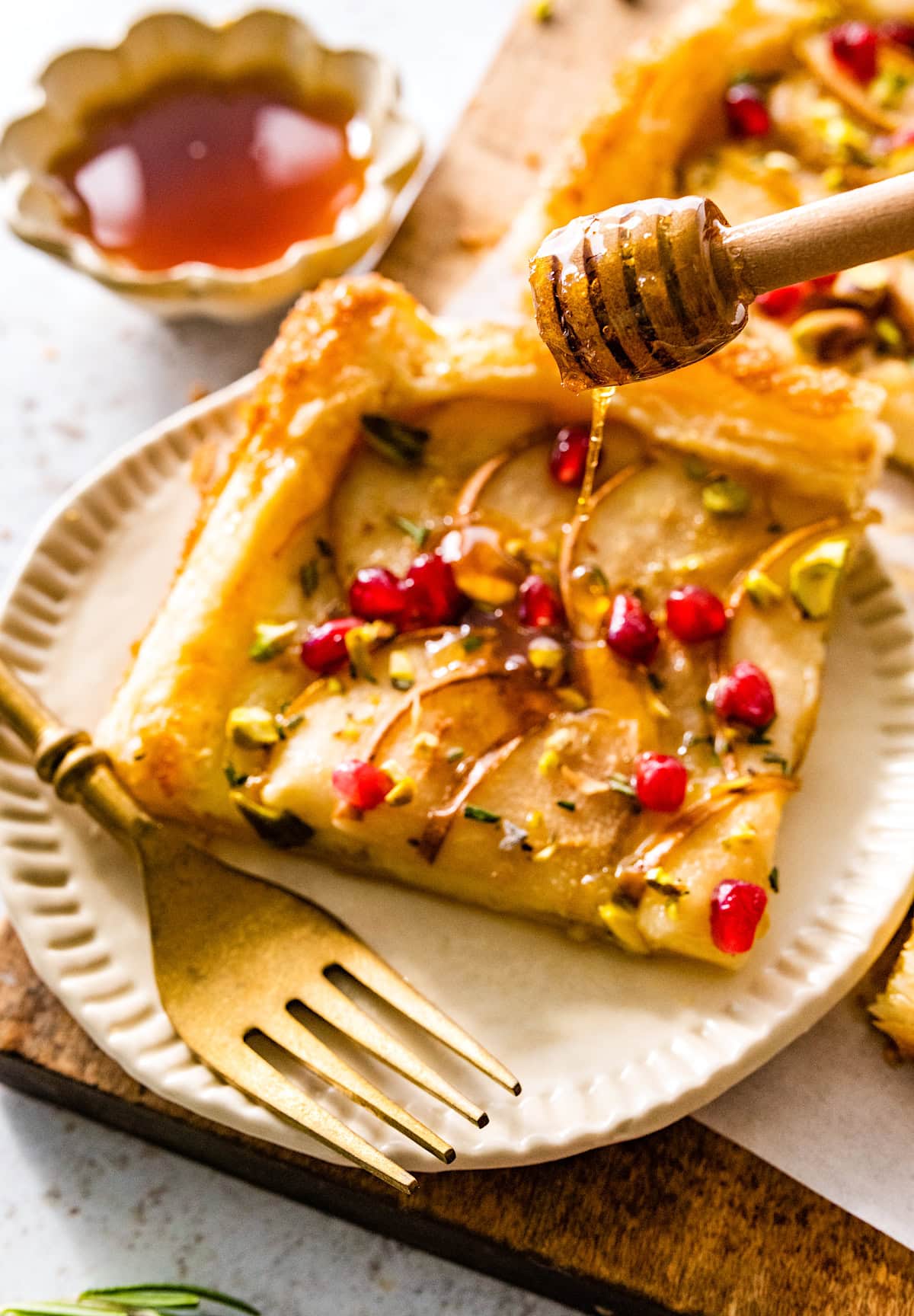 piece of pear brie puff pastry tart on plate with fork and honey being drizzled on top. 