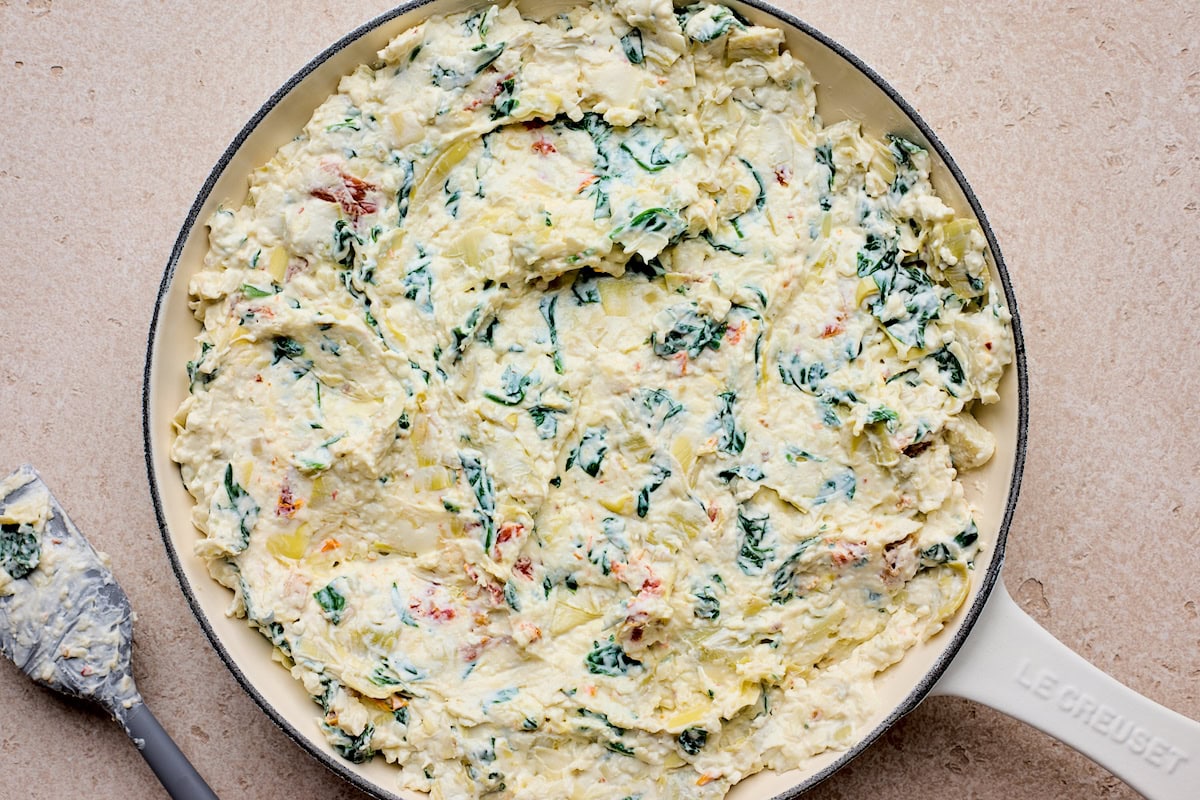 spinach artichoke sun-dried tomato dip spread in cast iron skillet. 