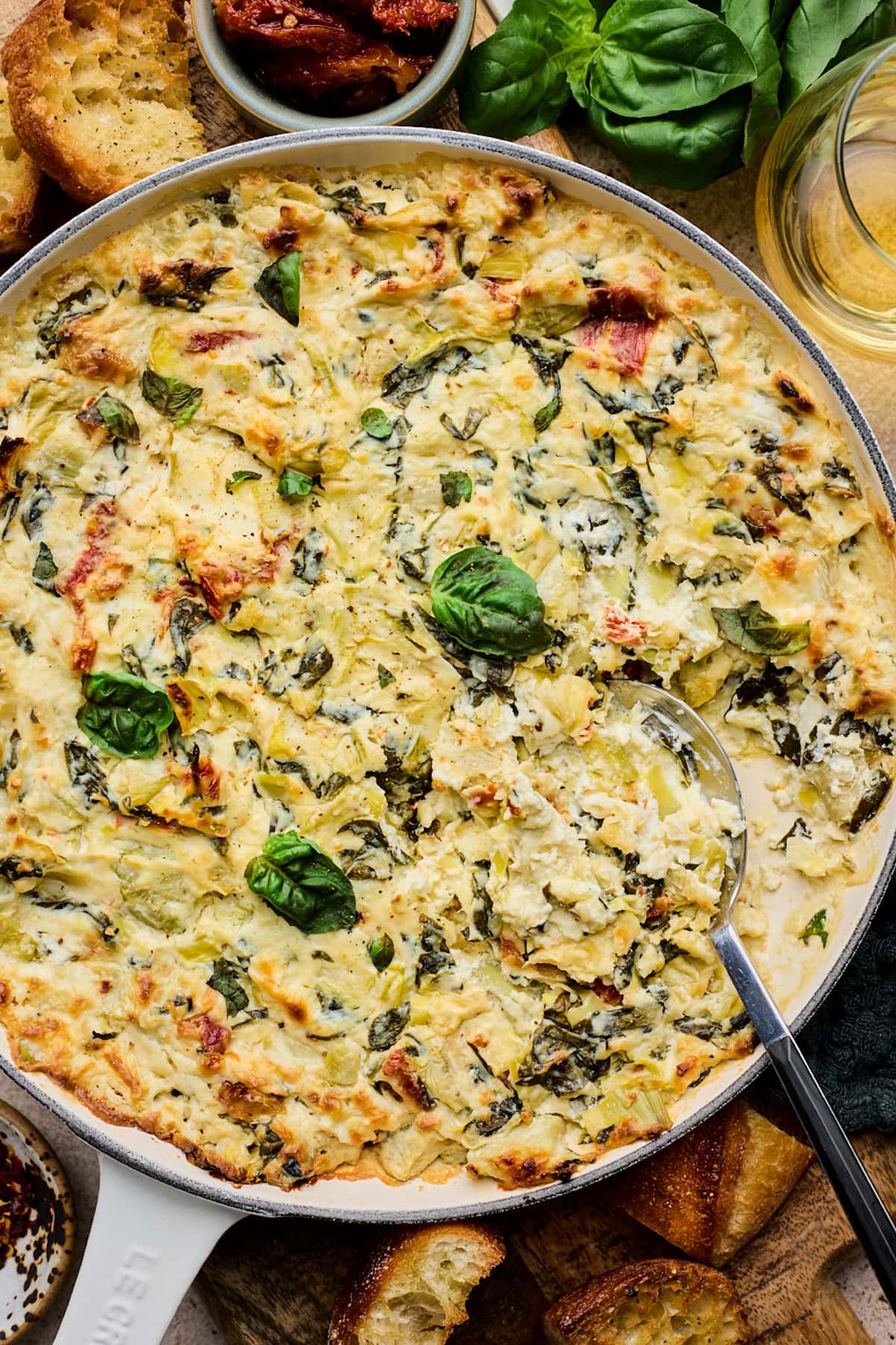 spinach artichoke sun-dried tomato dip with basil in cast iron skillet with spoon. 