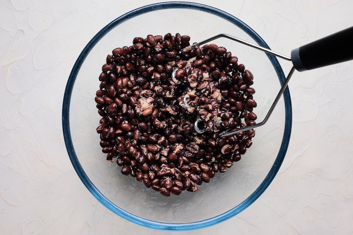 black beans in a bowl being mashed to make black bean burger. 