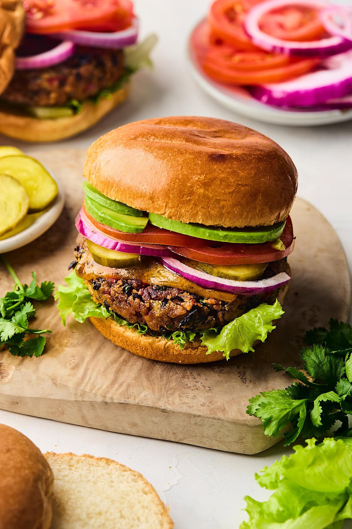 black bean burger on bun with avocado, tomato, pickles, red onion, cheese, and lettuce. 