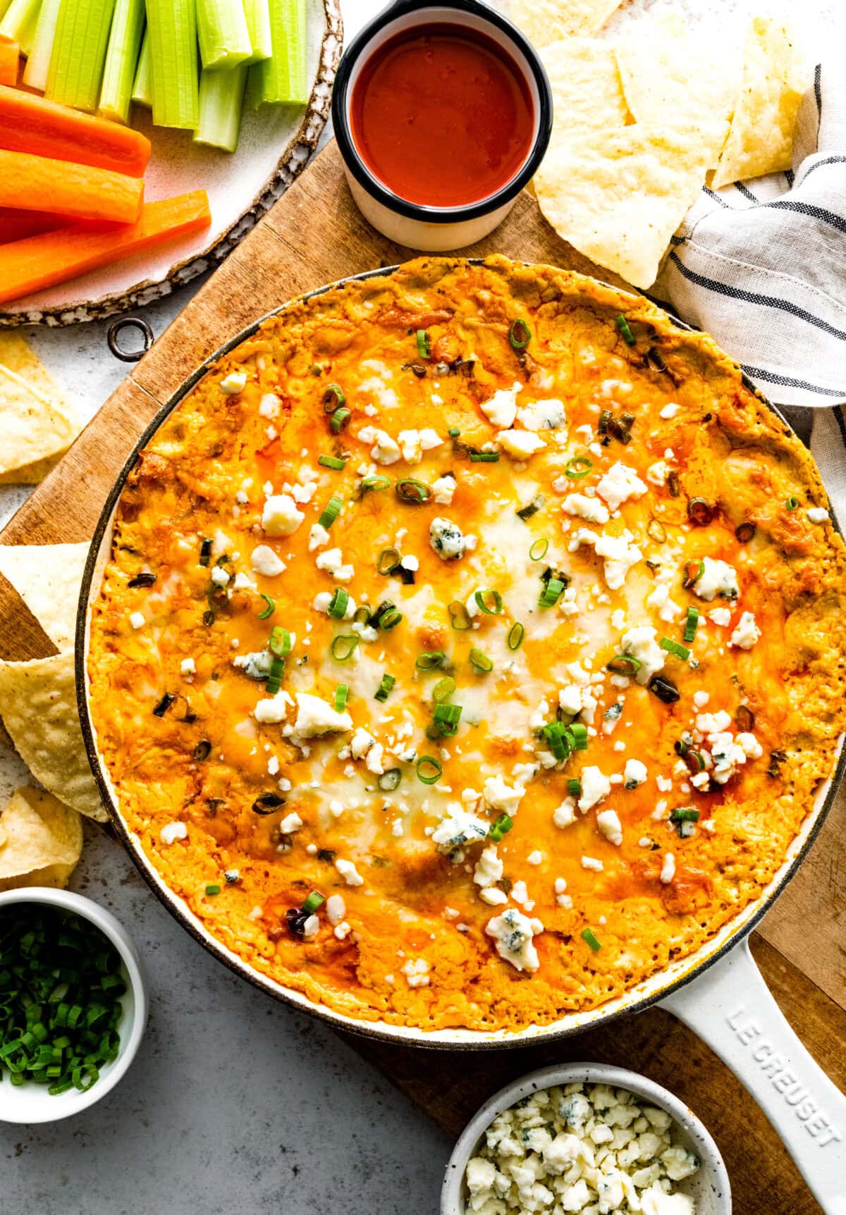 cheesy buffalo chicken dip in skillet with crumbled blue cheese, green onion, and tortilla chips. 