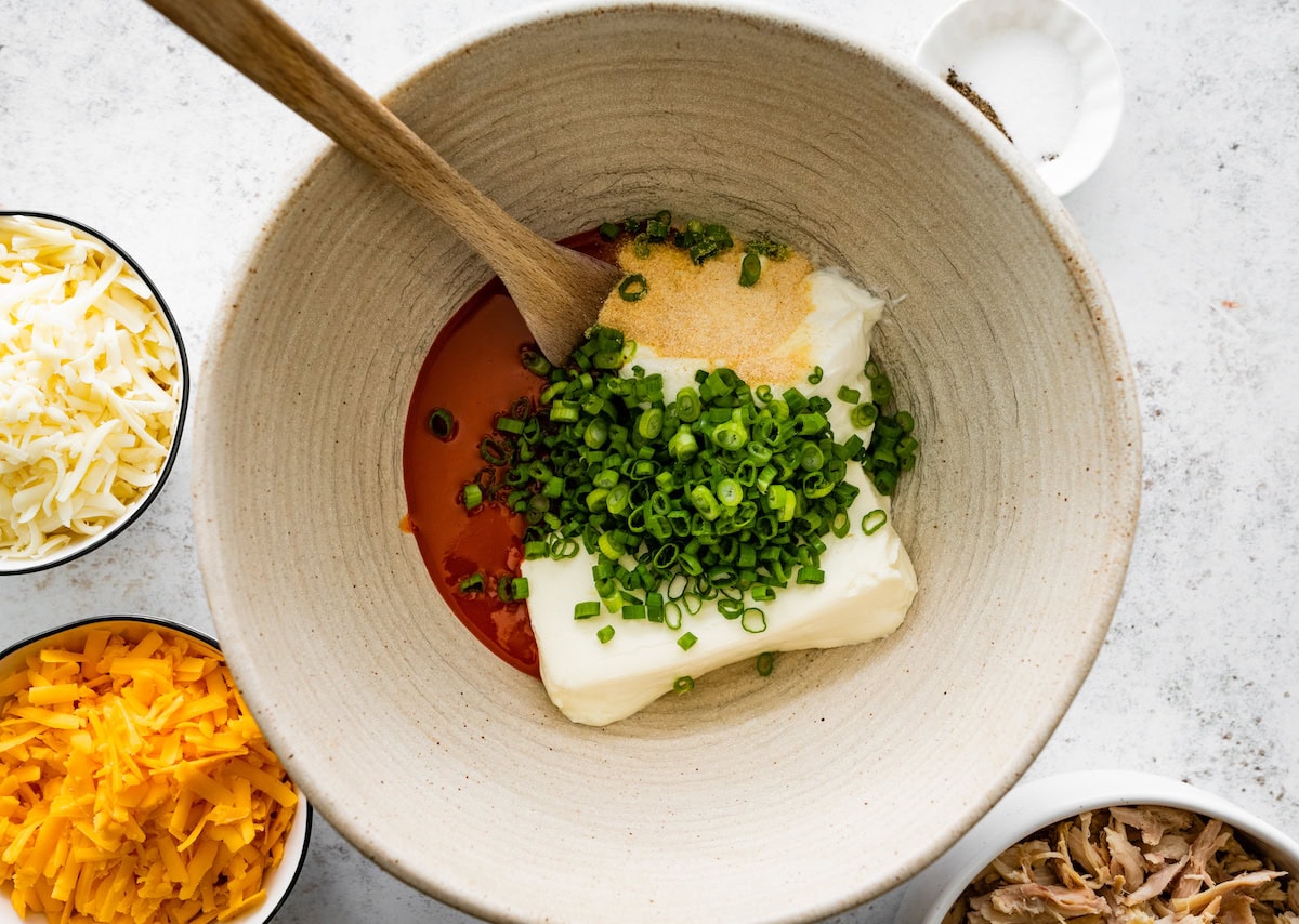 cream cheese, green onions, buffalo sauce, and seasonings in mixing bowl with wooden spoon. 