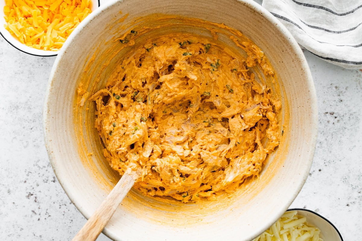 buffalo chicken dip mixture in mixing bowl with wooden spoon. 