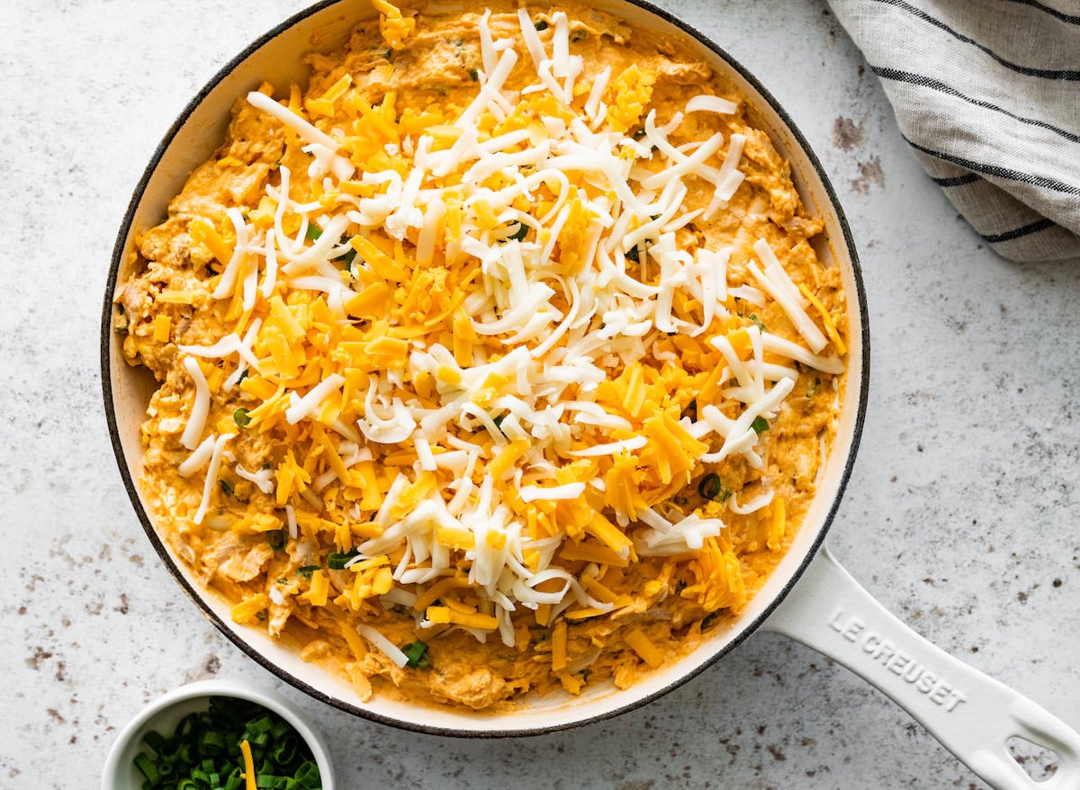 buffalo chicken dip in skillet with shredded cheese, ready to go into the oven. 