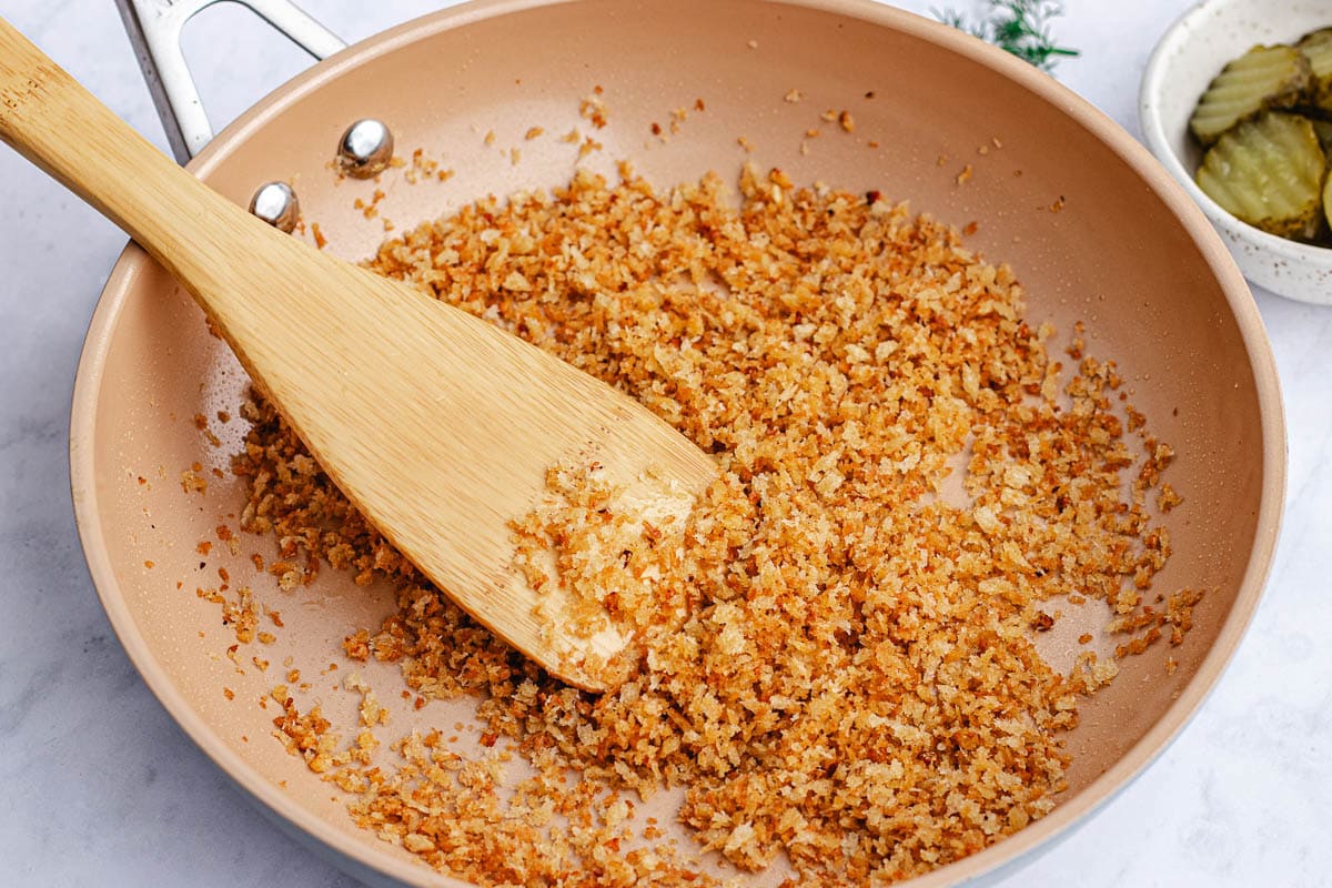 toasted garlic breadcrumbs in skillet with wooden spoon. 