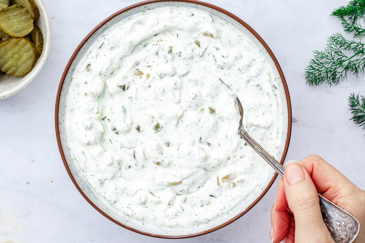 dill pickle dip in bowl being stirred with spoon. 