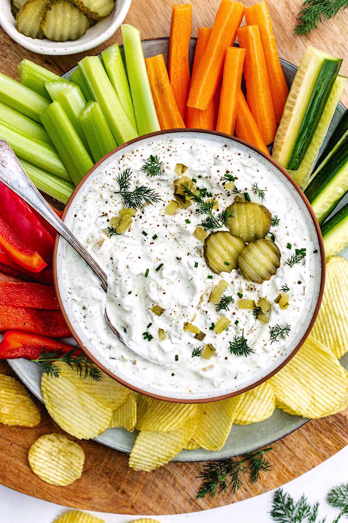 dill pickle dip on platter with potato chips and vegetables. 