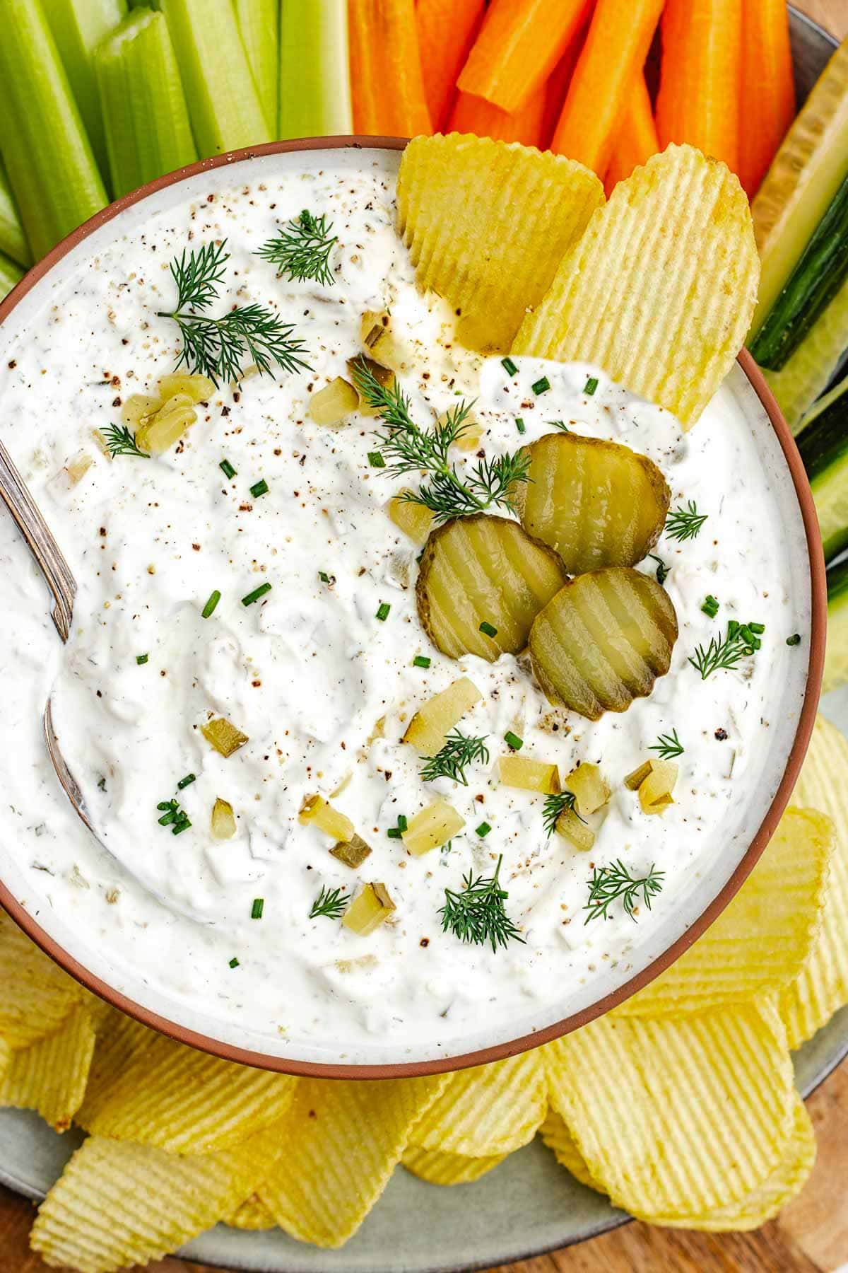 dill pickle dip in bowl with spoon and potato chips. 