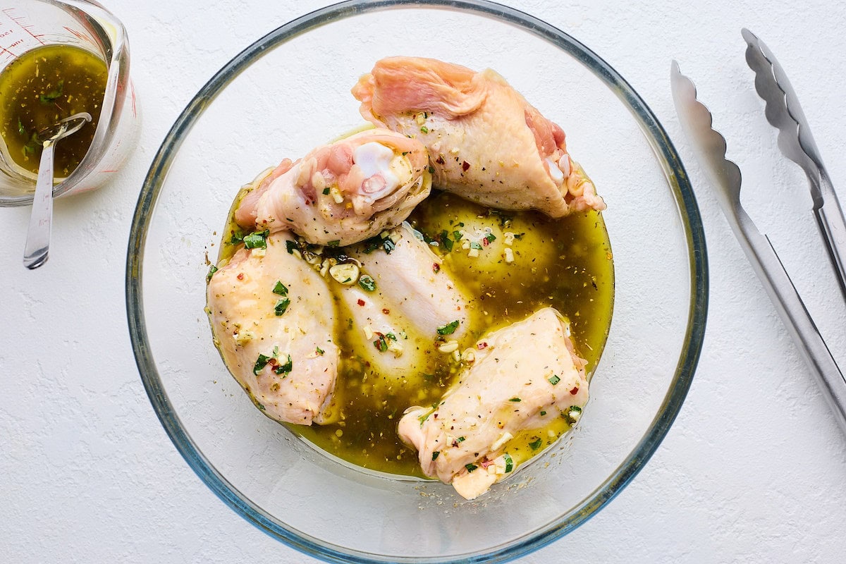 chicken thighs marinating in bowl to make Greek sheet pan chicken. 