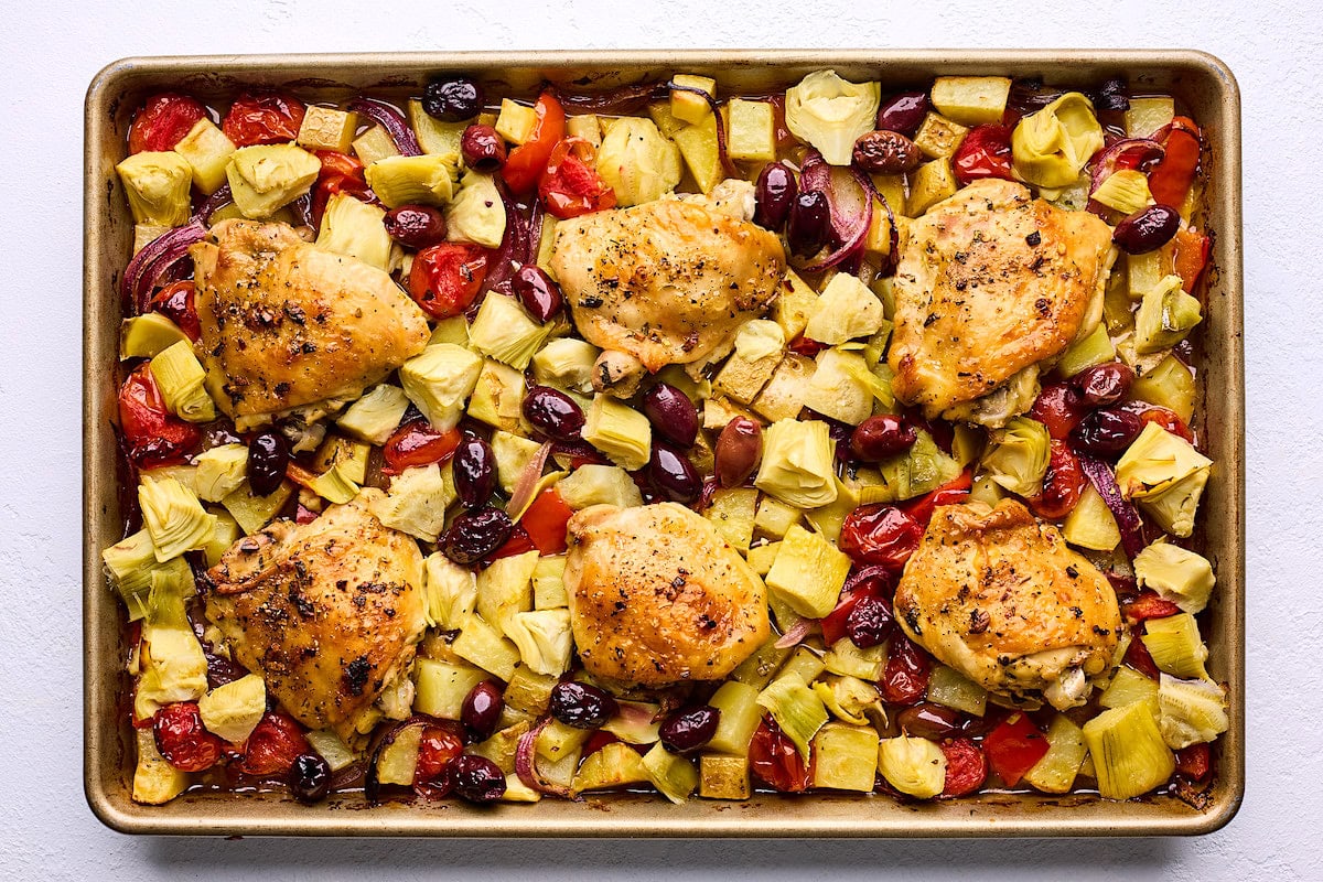 chicken thighs on sheet pan with artichokes, potatoes, red bell peper, tomatoes, red onion, and kalamata olives. 