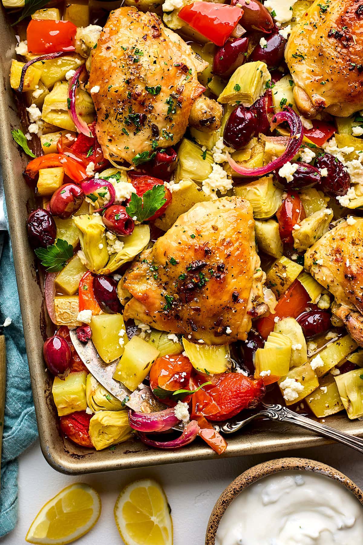 Greek sheet pan chicken on sheet pan with serving spatula. 