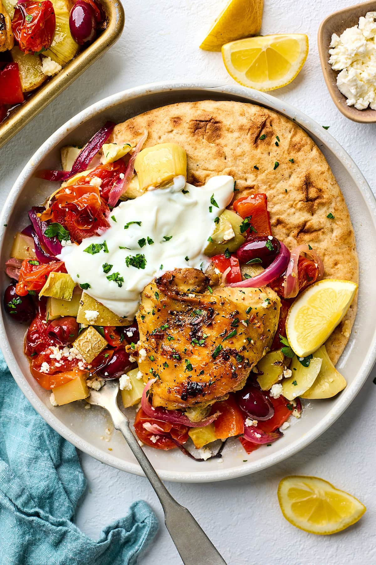 Greek chicken with vegetables on plate with tzatziki and pita bread. 