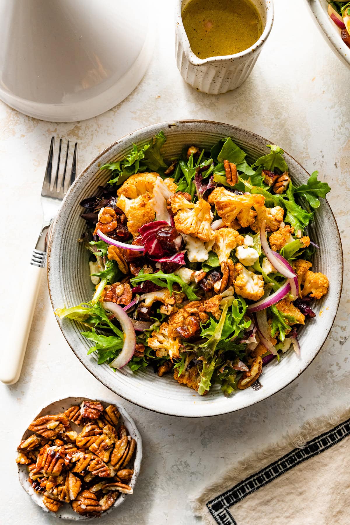 roasted cauliflower salad with dates, pecans, goat cheese, and red onion on plate. 