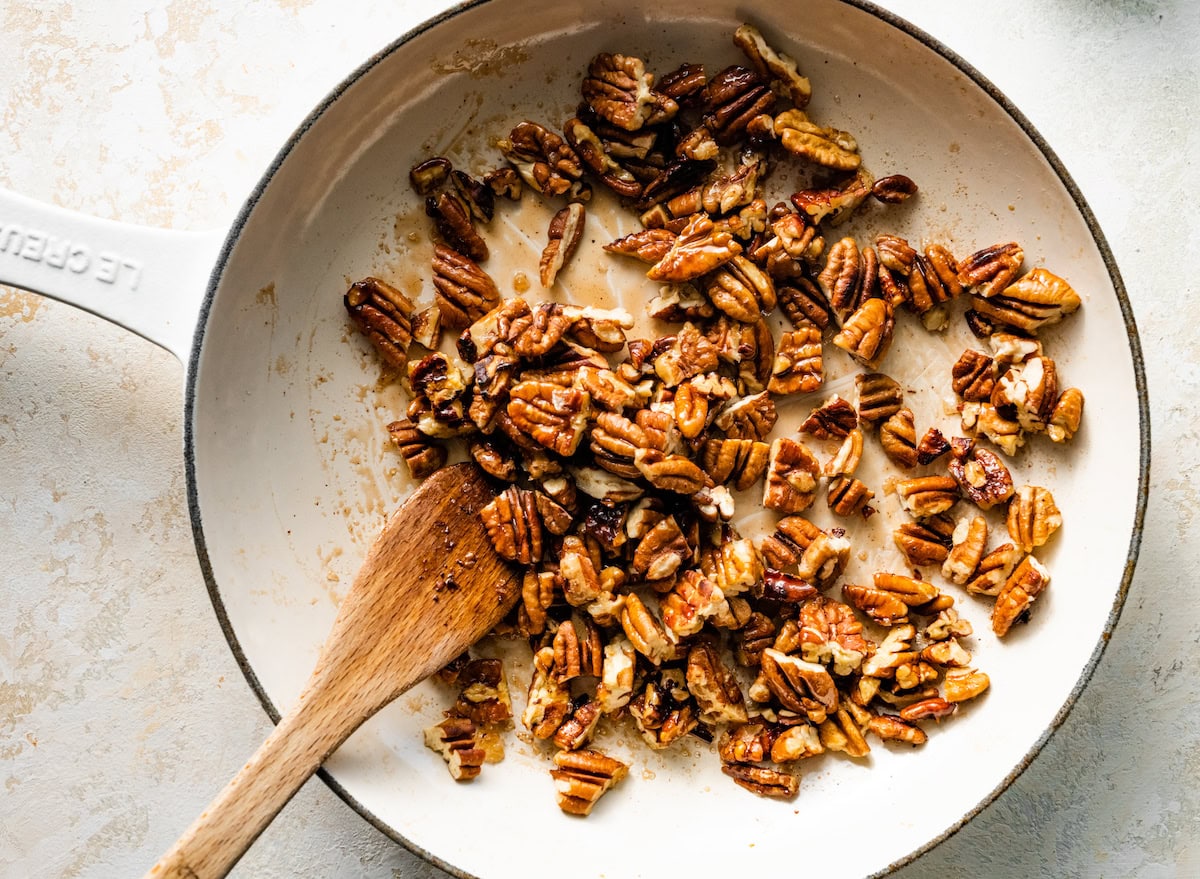 salted maple pecans cooking in skillet with wooden spoon. 