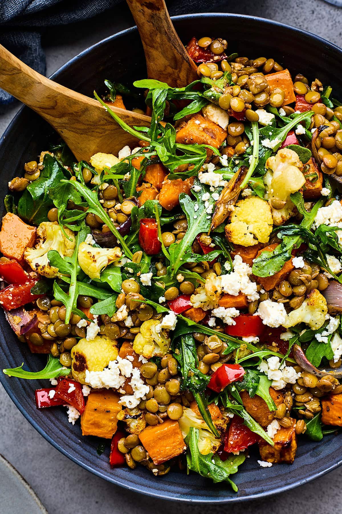 roasted vegetable lentil salad in bowl with wood salad servers. 