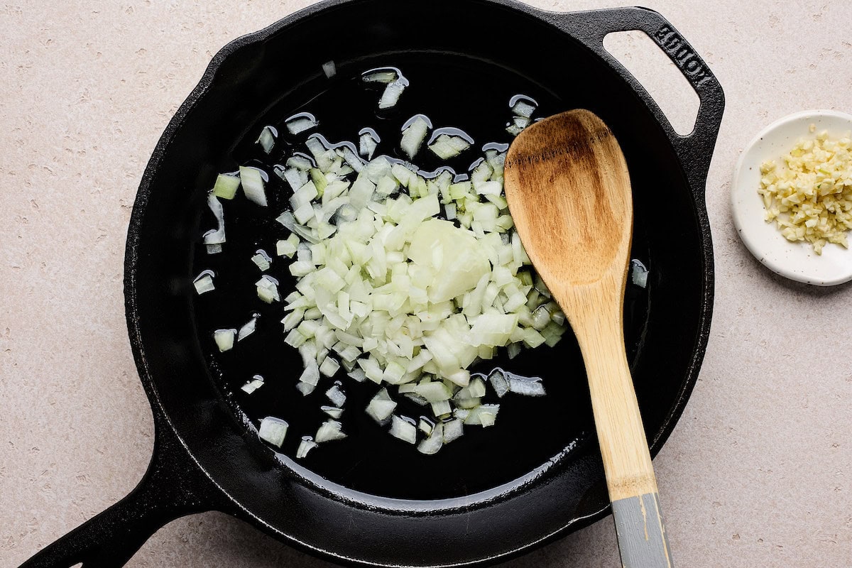 onion cooking in cast iron skillet with wooden spoon. 