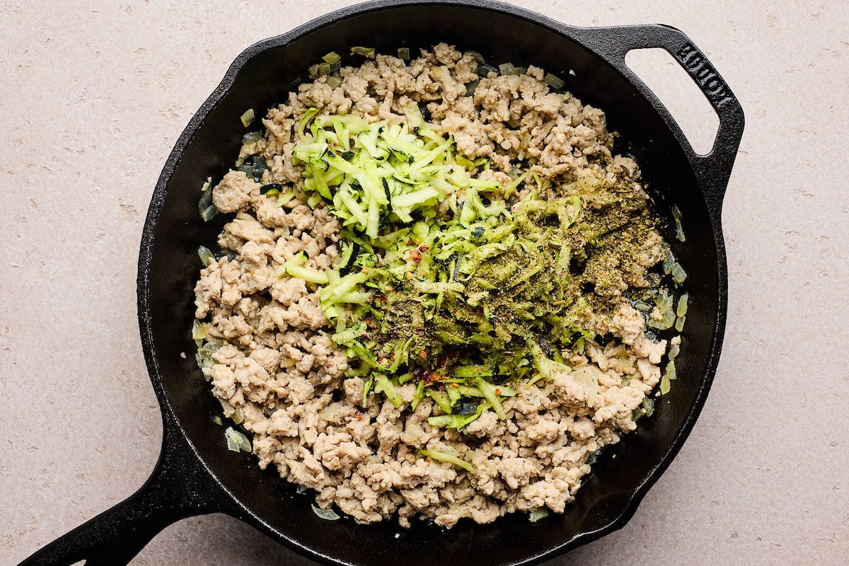 ground turkey cooking in skillet with shredded zucchini and spices. 