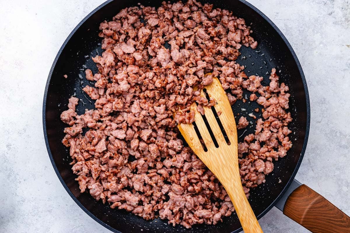 sausage cooking in skillet with wooden spoon. 