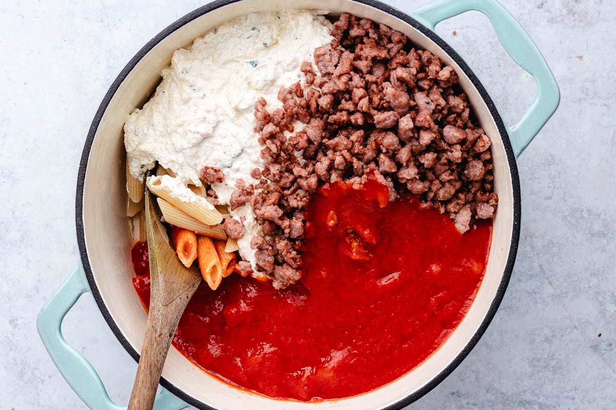 pasta, ricotta cheese mixture, sausage, and marinara sauce being combined in large pot with wooden spoon. 