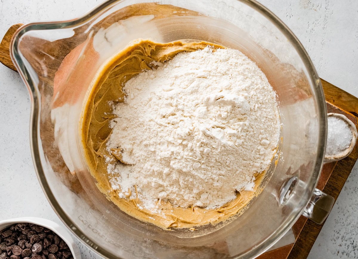 dry ingredients being added to wet ingredients in mixing bowl to make chocolate chip cookie bars. 