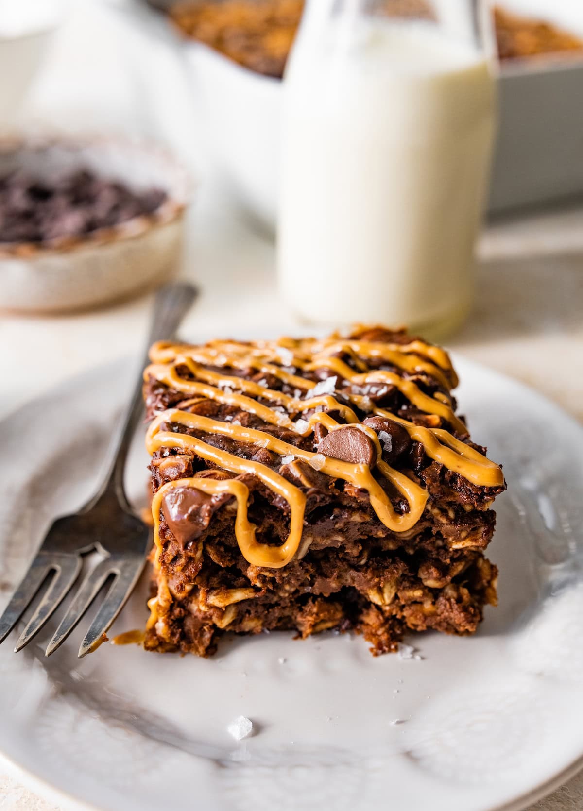 piece of chocolate peanut butter baked oatmeal with peanut butter drizzle and flaky sea salt on plate with fork. 