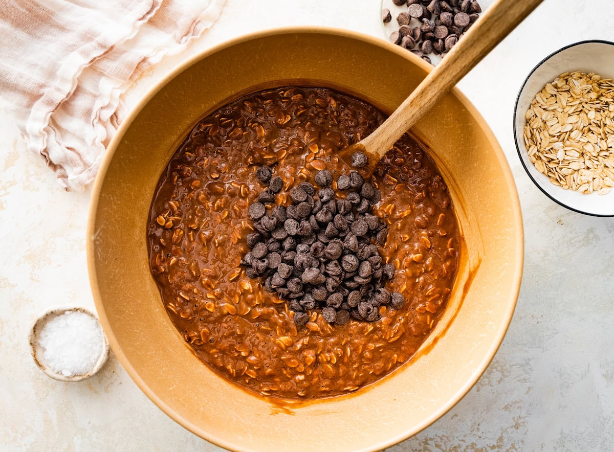 chocolate peanut butter baked oatmeal mixture in mixing bowl with chocolate chips in mixing bowl with spatula. 