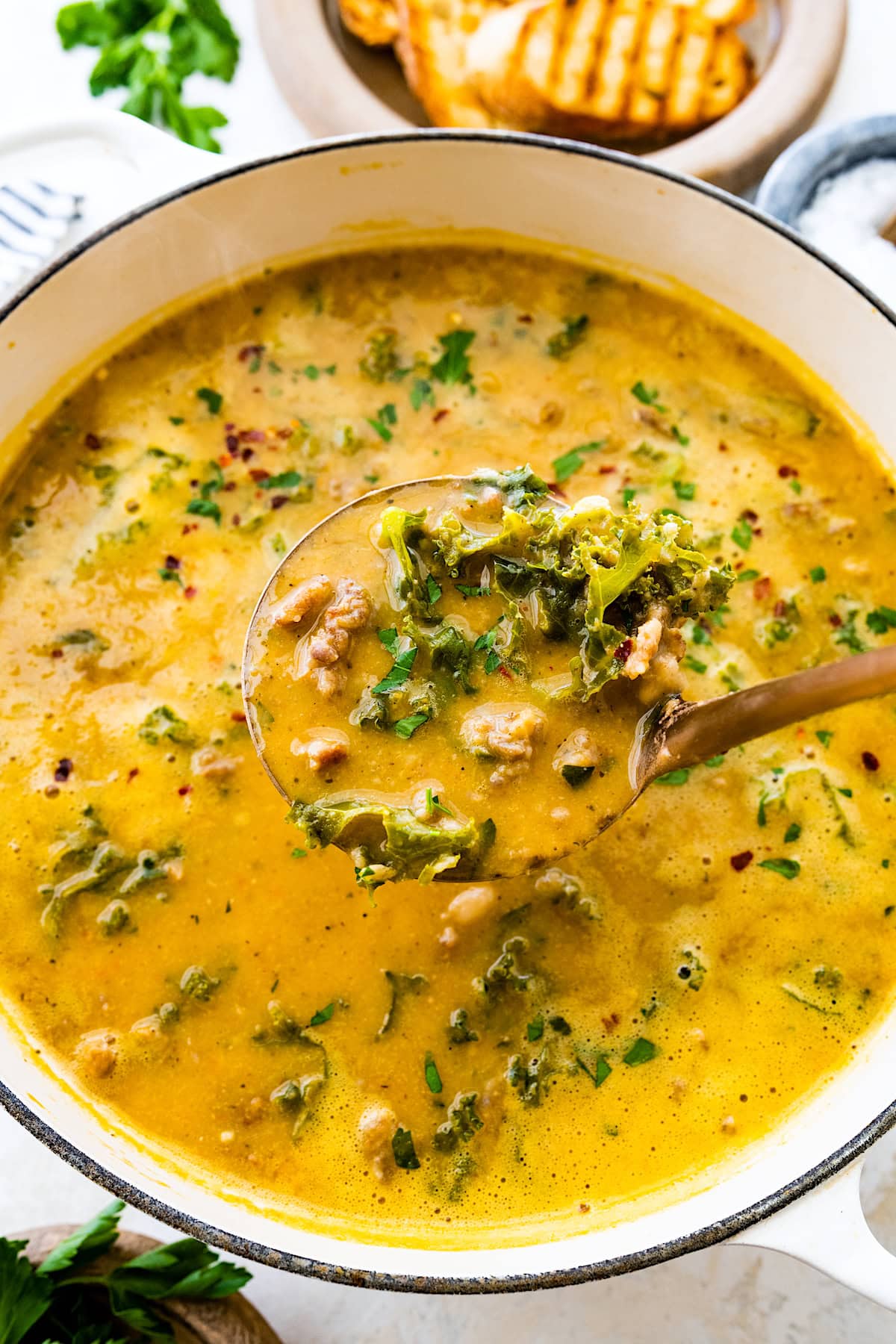 sausage kale white bean soup with in pot with fresh herbs. 