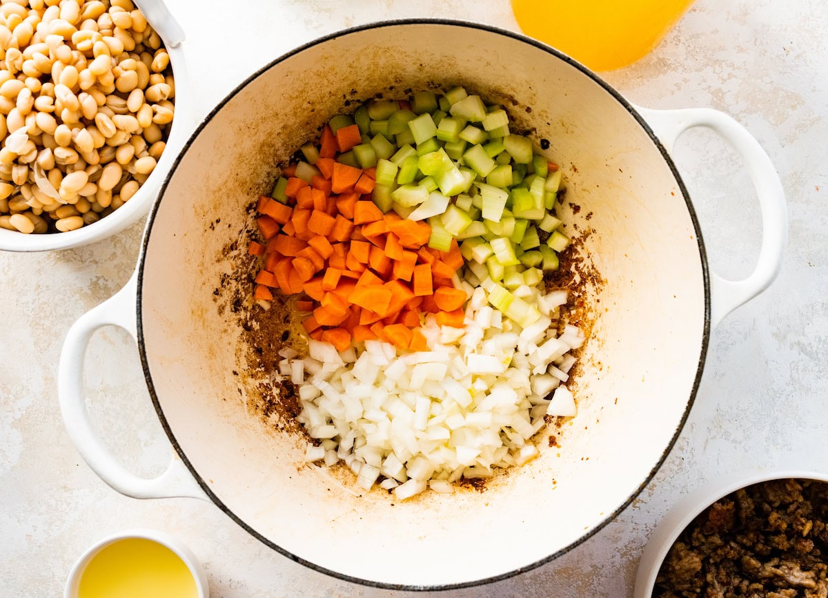 carrots, celery, and onion cooking in white pot. 