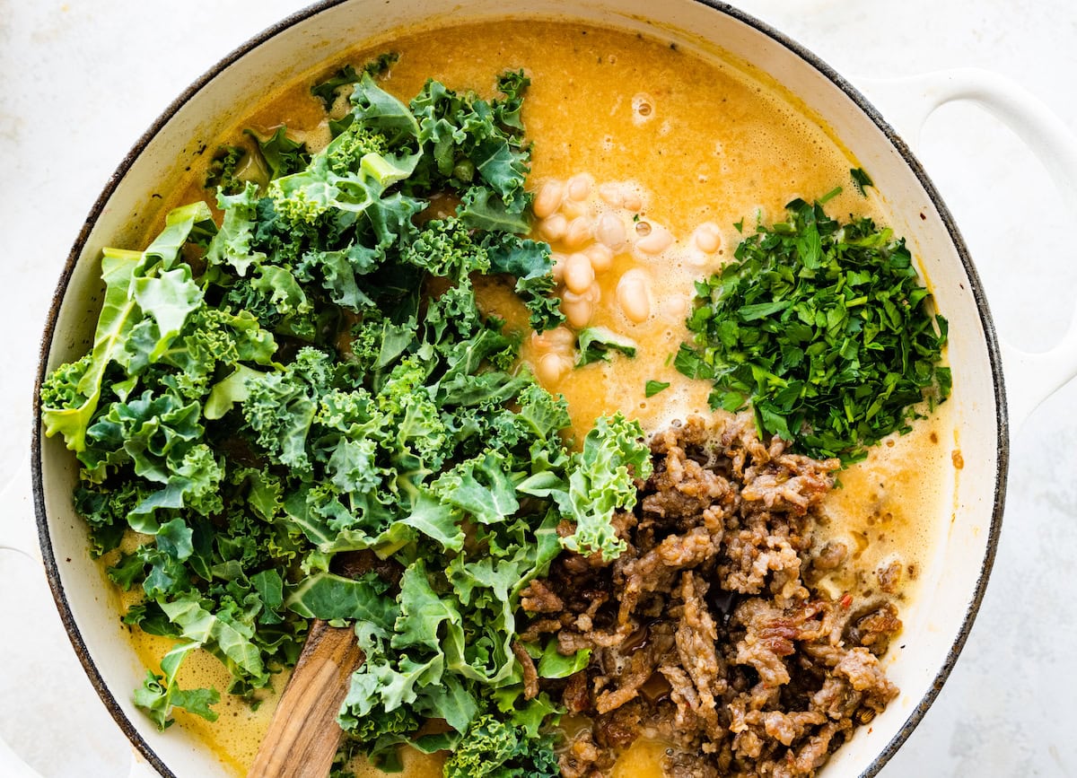 kale, sausage, and parsley being added to soup. 