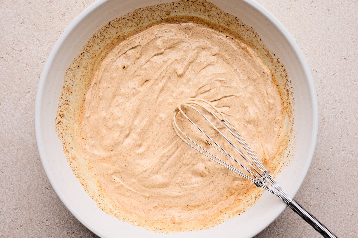 creamy Greek yogurt dressing with taco seasoning in bowl with whisk. 