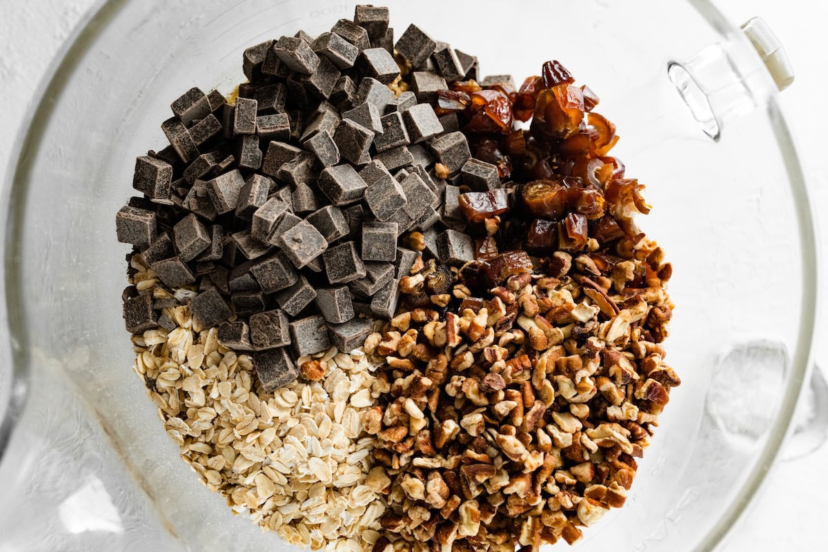 chopped pecans, dates, and chocolate chunks being added to oatmeal cookie dough. 