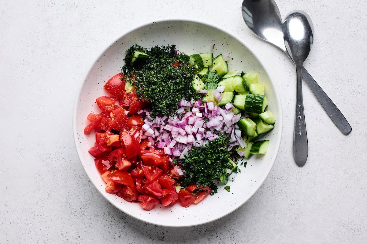 tomato, cucumber, red onion, and fresh herbs in bowl. 