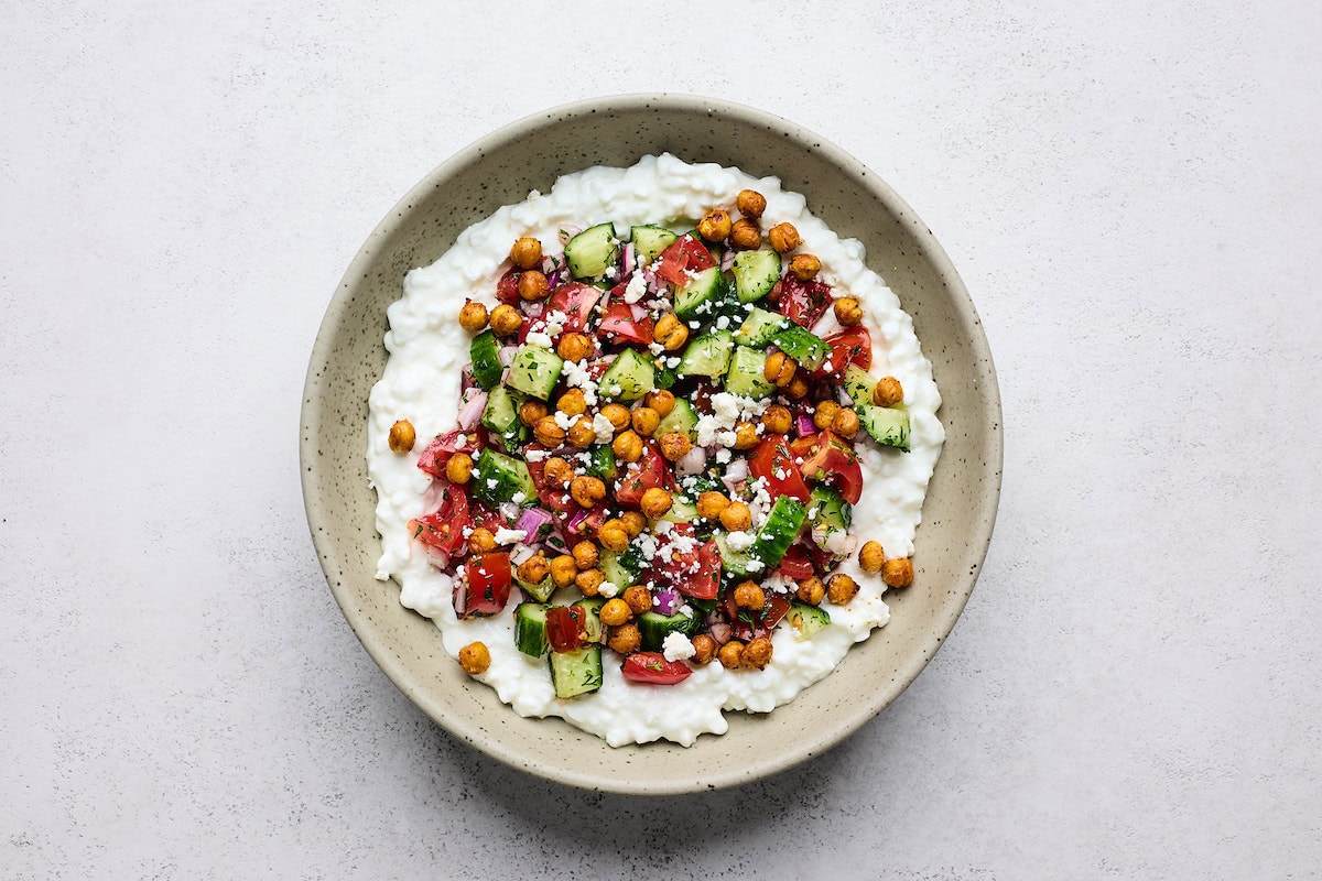 cottage cheese salad in bowl with crispy chickpeas, tomato, cucumber, red onion, and feta on top. 