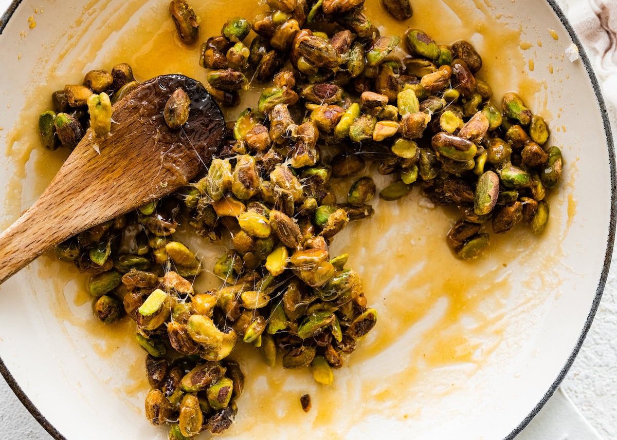 pistachios coated in sugar and honey in skillet with wooden spoon to make candied pistachios. 