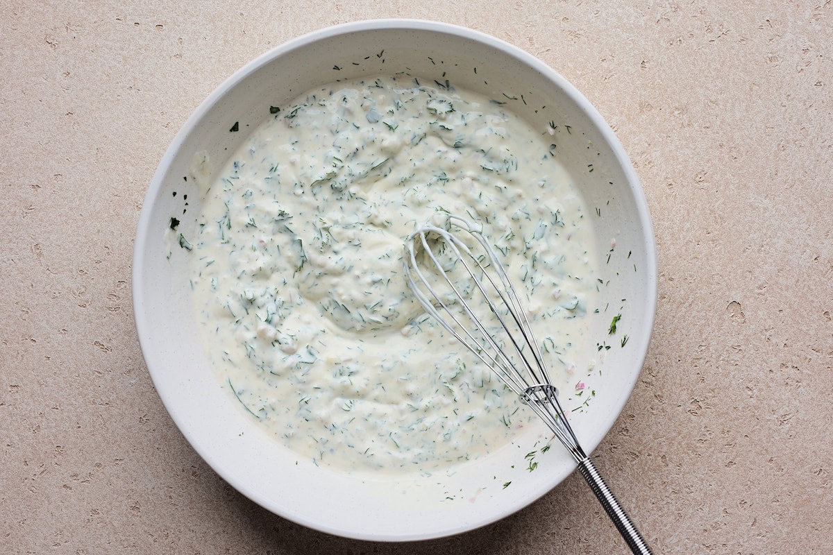 creamy Greek yogurt herb dressing in bowl with whisk for smashed potato salad. 