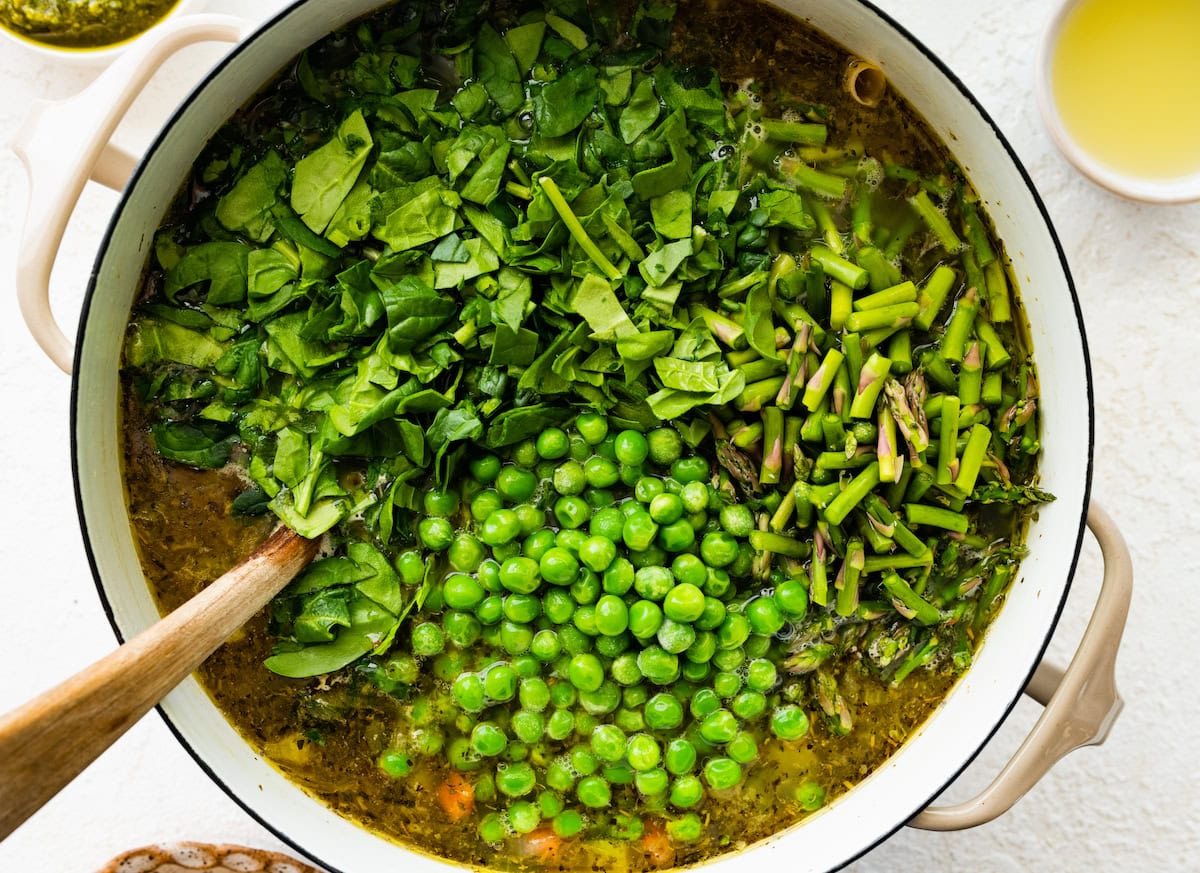 spinach, asparagus, and peas being added to spring minestrone soup. 